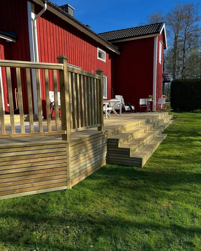 Nybyggd altan med trappa och räcke vid ett rött hus