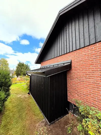 Tillbyggnad med svart träpanel mot tegelhus