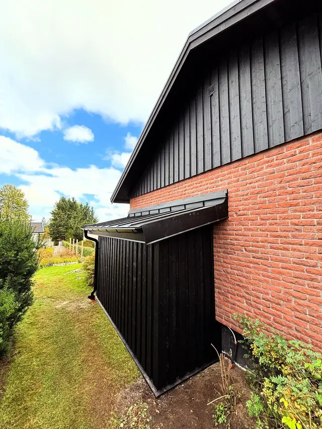 Tillbyggnad med svart träpanel mot tegelhus
